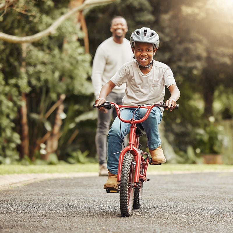 Kid rides bike while adult looks on